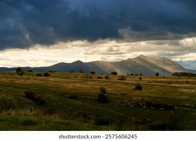 Sunbeams streaming through clouds illuminate a majestic mountain range rising over a vast grassland at sunset, creating a stunning and tranquil landscape filled with natural beauty