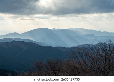 Sunbeams streaming through clouds over layered mountain ridges at Mount Kongō, Chihaya Enchi Observatory, Osaka, Japan, captured in winter scenery perfect for travel, nature, and landscape projects.
