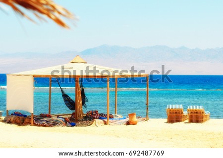 Sunbeds, hammock & simple tent at sandy beach by the seaside. Red Sea in Egypt (Nuweiba bedouin village). Bright summer sunny colors. Tranquil & chilling out day.