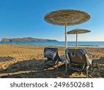 Sunbeds on a sandy beach with towels protected by a parasol against the hot Greek sun. A beach in the resort of Agia Marina, Crete, Greece.