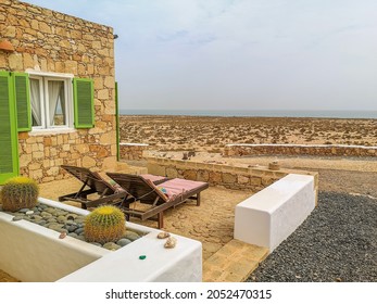 Sunbeds in terrace of an old stone house with majestic desert view. Boa Vista Island, Cape Verde, Africa. Selective focus on the building exterior, blurred background. - Shutterstock ID 2052470315