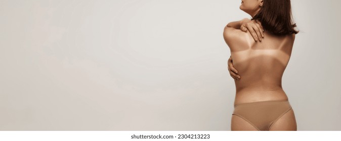 Sunburn marks. Back view image of slim woman, girl with swimwear tan line over light studio background. Sun protection cosmetics. Concept of health, spf, sunscreen lotion, vacation, summer, ad