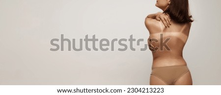 Sunburn marks. Back view image of slim woman, girl with swimwear tan line over light studio background. Sun protection cosmetics. Concept of health, spf, sunscreen lotion, vacation, summer, ad