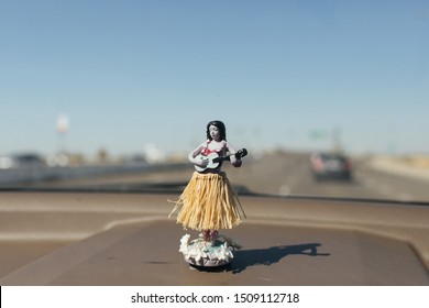 Sun-burnt Hawaiian Hula Dancer Air Freshener Figurine On A Dashboard Of A Car.