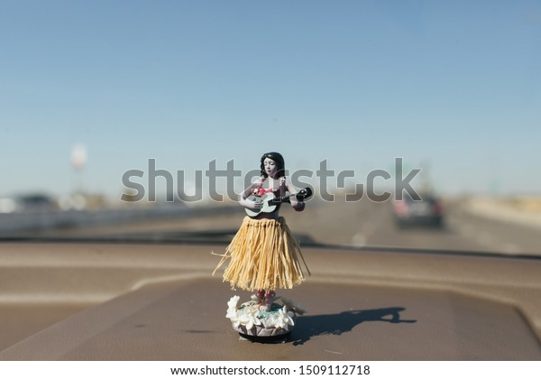 Sun-burnt Hawaiian hula dancer air freshener\
figurine on a dashboard of a\
car.