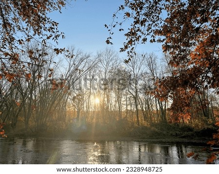 sunburst shining on the river with trees with fall leaves