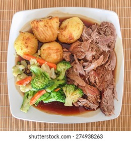 Sunday Lunch Meal Of Roast Lamb, Roast Potatoes, Gravy And Vegatables On A White Plate From Above.