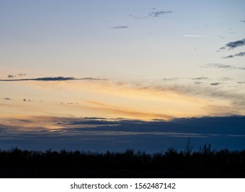 Sundown At The Countryside. Twilight Landscape. Blue And Yellow Clouds And Silhoutte Of Trees. Airplane In The Sky. 