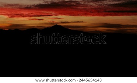 Sundown with a desert sky set aflame over distant silhouetted mountains and brilliantly hued and vivid colors.