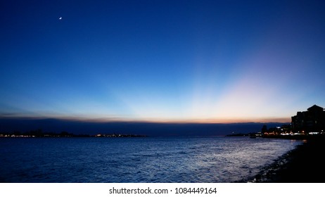 Sundown at Pier, sun rays hiding behind the horizon and the reflection on the water, the Moonlight and some city lights.