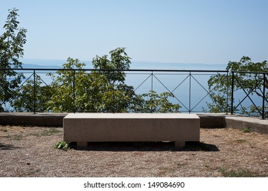 A sun-drenched bench sits on an elevated panoramic point on the via Napoleonica in Trieste, Italy