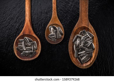 Sunflower Seeds Overhead Organic Roasted And Salted Close-up Arrangement In Three Old Brown Wooden Spoons On Black Shiny Stone Background Studio Shot