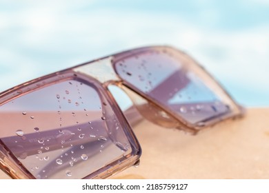 Sunglasses Against The Cloudy Sky Or On Edge Of The Pool,blue Water In Background.water Drops On Glass.summer Vacation,sea,beach Concept,relaxation,tan.eye Protection From Uv Rays.sparkling Pool,sun