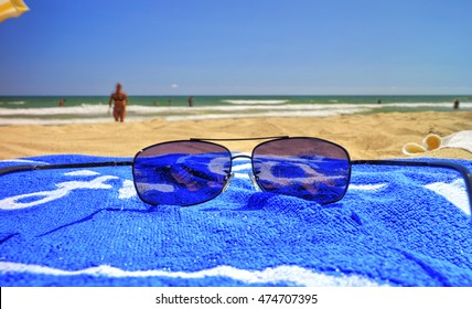 Sunglasses And Blue Towel On The Sandy Beach