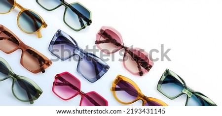 Sunglasses composition in many bright colors in transparent plastic. Top view with shadow. Trendy glasses isolated on white background. Glasses with polarized lenses. Fashionable eyewear for women.