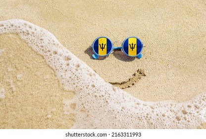 Sunglasses With Flag Of Barbados On A Sandy Beach. Nearby Is A Sea Lightning And A Painted Smile. The Concept Of A Successful Vacation In The Resorts Of The Barbados.