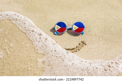 Sunglasses with flag of Philippines on a sandy beach. Nearby is a sea lightning and a painted smile. The concept of a successful vacation in the resorts of the Philippines.