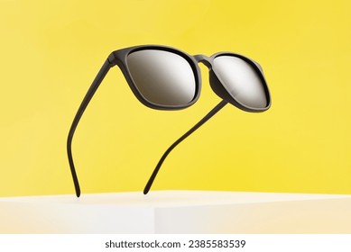 Sunglasses float in air above white square podium.