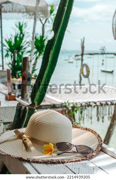 A Sunglasses and floppy straw hat on the desk inf\
front of beach in Bali