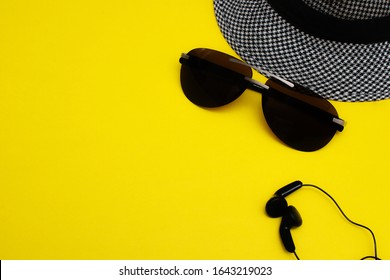 Sunglasses, A Man's Hat And Headphones. Summer And Staycation Concept, Creative Layout On A Yellow Background, Top View, Copy Space