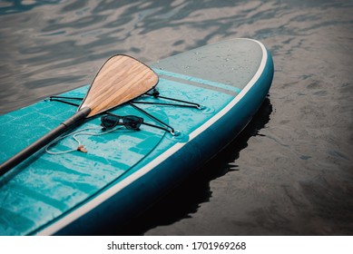 Sunglasses on a blue stand up paddle board in the water with a paddle