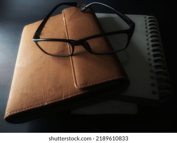 Sunglasses On A Leather-bound Book. With Black Background.painting Light.close Up.