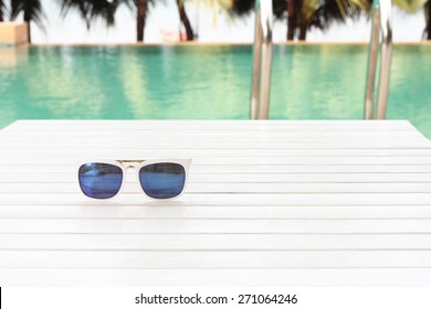 sunglasses on wooden table by the pool
