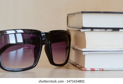 Sunglasses with a reflection of the window and a stack of books at an angle. Snapshot krypnom plan. A set of items for reading on vacation
