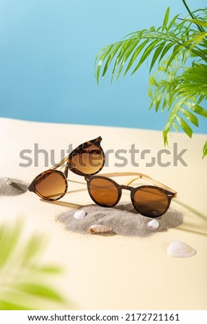 Sunglasses sale concept. Trendy sunglasses on beach with green palm leaves. Trendy Fashion summer accessories. Side view, copy space. Optic store. Vacation, travel concept. Sunglass offer poster