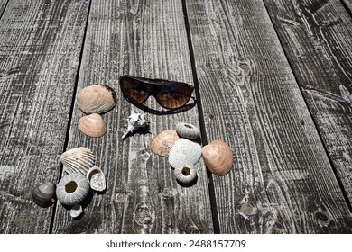 Sunglasses and seashells lying on a rustic wooden surface, evoking summer holiday memories.