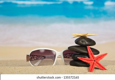 Sunglasses, starfishes and pebbles on sand - Powered by Shutterstock