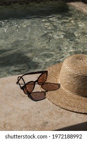 Sunglasses and straw hat on marble swimming pool side with clear blue water with waves sunlight shadow reflections. Minimal fashion aesthetic summer vacation creative background