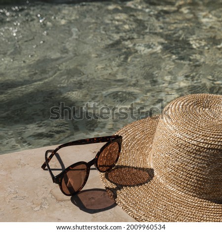 Sunglasses and straw hat on marble swimming pool side with clear blue water with waves sunlight shadow reflections. Minimal fashion aesthetic summer vacation creative background 商業照片 © 