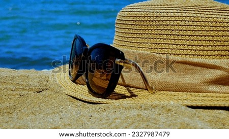 Sunglasses and a straw hat on the sand against the background of the sea. The concept of recreation by the sea