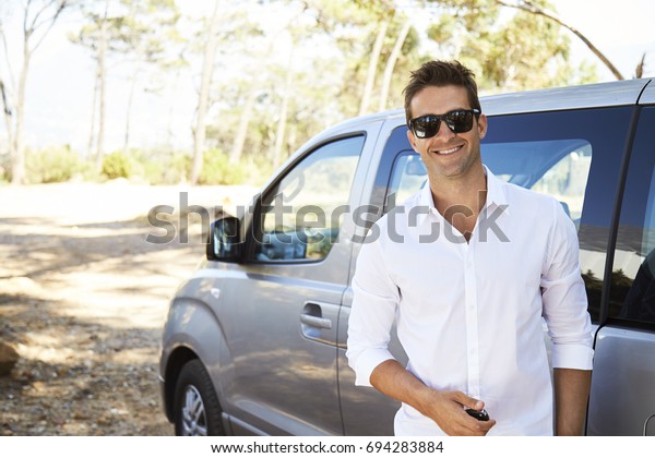 Sunglasses and white\
shirt guy smiling by\
car