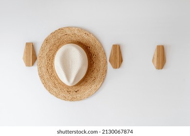 Sunhat on hanger for clothes in hall. Close up view of brimmed hat hanging on wooden hook for apparel on white copy space wall in room - Powered by Shutterstock