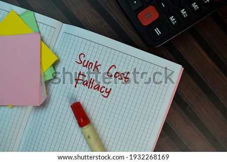Sunk Cost Fallacy write on a book isolated on Wooden Table.