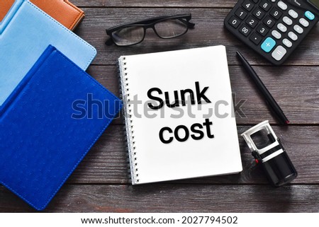 SUNK COST text on notebook with eyeglasses, calculator, stamp and pen on a wooden background. Flat lay.