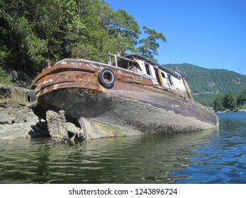 Sunken boat on the rocks at Pender Harbour BC, Canada. The boat is resting in a tilted position on the shoreline of a small island. The degree of the disrepair suggests it has been here for some time.