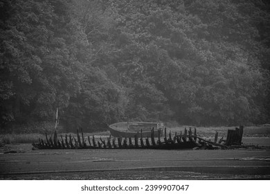 Sunken ships stranded on the beach with low tide and orange and green algae on rainy day black and white BW - Powered by Shutterstock