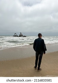 Sunken Trawler, Shipwreck. A Stranded Ship. Old Rusty Metal Ship. Zeila At The Skeleton Coast In Namibia. Atlantic Ocean Off The Coast Of Africa. Man Stands And Looks At The Beach.