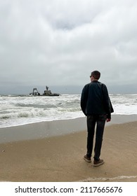 Sunken Trawler, Shipwreck. A Stranded Ship. Old Rusty Metal Ship. Zeila At The Skeleton Coast In Namibia. Atlantic Ocean Off The Coast Of Africa. Man Stands And Looks At The Beach.