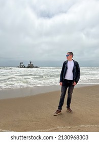 Sunken Trawler, Shipwreck. A Stranded Ship. Old Rusty Metal Ship. Zeila At The Skeleton Coast In Namibia. Atlantic Ocean Off The Coast Of Africa. Man Stands And Looks At The Beach.