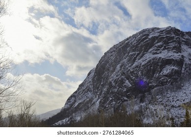 Sunlight Breaking Over Snowy Mountain Cliff with Blue Lens Flare