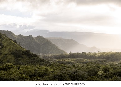 Sunlight breaking through clouds over a green mountain near Hana, Maui