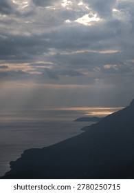 Sunlight breaking through dense clouds above a calm body of water, creating a serene and spiritual natural atmosphere.