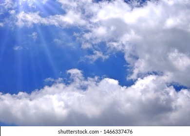 Sunlight breaking through white clouds, blue sky background.