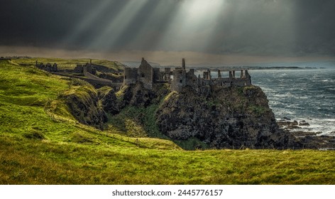 Sunlight breaks through clouds above the Dunluce Castle ruins near Dunluce Road, Bushmills, Northern Ireland, United Kingdom.