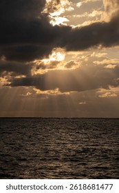 Sunlight breaks through clouds over the ocean during evening hours