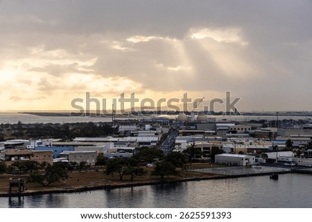 Sunlight breaks through clouds over industrial coastal city in Honolulu, Hawaii.
